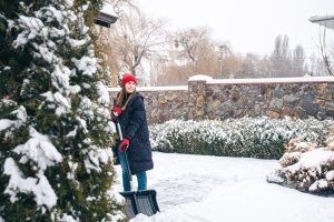 young woman cleans snow with hand shoveling tools
